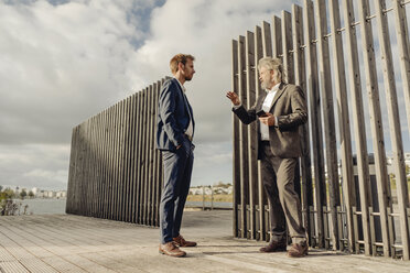 Two businessmen standing on jetty at a lake talking - KNSF03359