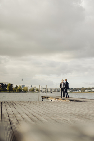 Zwei Geschäftsleute stehen auf einem Steg an einem See und unterhalten sich, lizenzfreies Stockfoto