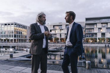 Two businessmen talking at city harbor at dusk - KNSF03375