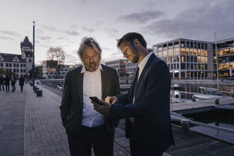 Zwei Geschäftsleute mit Mobiltelefon am Stadthafen in der Abenddämmerung, lizenzfreies Stockfoto