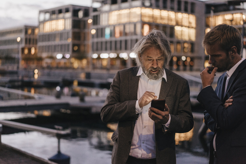 Zwei Geschäftsleute mit Mobiltelefon am Stadthafen in der Abenddämmerung, lizenzfreies Stockfoto