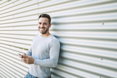 Porträt eines lachenden Mannes mit Smartphone - RAEF01954