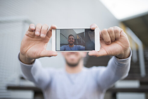 Lächelnder Mann, der ein Selfie mit seinem Mobiltelefon macht, Nahaufnahme - RAEF01958