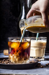 Hand gießt hausgemachte Kaffeeweißer mit Vanillegeschmack in ein Glas mit Eiskaffee - SBDF03424