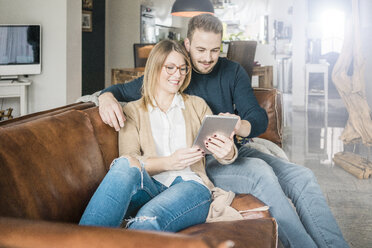 Smiling couple sitting on couch at home sharing tablet - MOEF00581