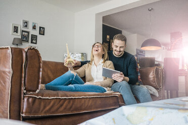 Happy couple sitting on couch at home with tablet and Eiffel tower model - MOEF00582