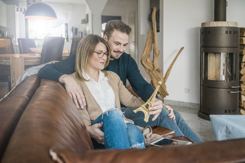 Lächelndes Paar sitzt zu Hause auf der Couch mit Tablet und Eiffelturm-Modell, lizenzfreies Stockfoto