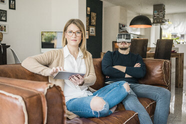 Couple sitting on couch at home with tablet and VR glasses - MOEF00585