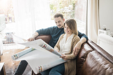 Couple sitting on couch at home looking at world map - MOEF00590