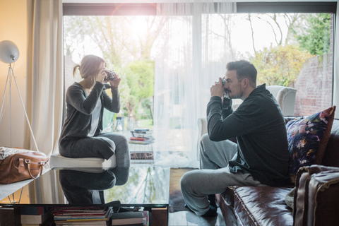 Paar im Wohnzimmer zu Hause, das sich gegenseitig fotografiert, lizenzfreies Stockfoto