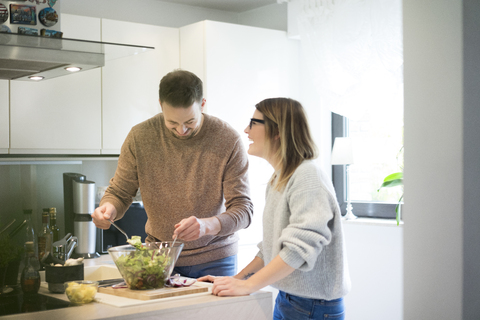 Glückliches Paar bereitet gemeinsam Salat in der Küche zu, lizenzfreies Stockfoto