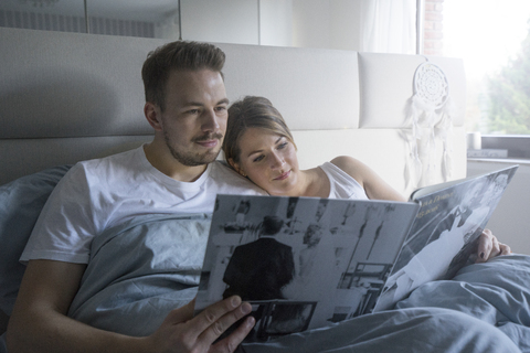 Ehepaar im Bett zu Hause mit Blick auf den Hochzeitskatalog, lizenzfreies Stockfoto