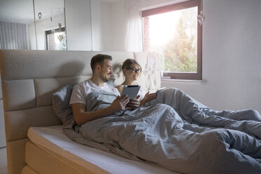 Lächelndes Paar im Bett zu Hause mit Tabletten - MOEF00608