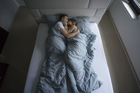 Draufsicht auf ein Paar, das zu Hause im Bett liegt und sich küsst - MOEF00612