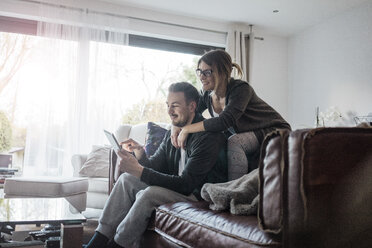 Lächelndes Paar, das zu Hause auf der Couch sitzt und ein Tablet benutzt - MOEF00622