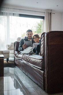 Lächelndes Paar, das zu Hause auf der Couch liegt und sich ein Tablet teilt - MOEF00624