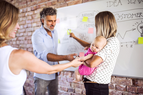 Colleagues caressing baby of working motherin office stock photo
