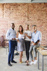 Portrait of smiling colleagues at desk in loft office - HAPF02620