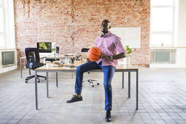Happy businessman with basketball at desk in office - HAPF02621