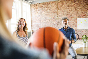 Lächelnde Kollegen mit Basketball im Büro - HAPF02622