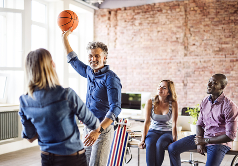 Colleagues playing basketball in office stock photo