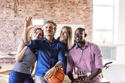Glückliche Kollegen mit Basketball im Büro machen ein Selfie, lizenzfreies Stockfoto