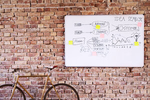 Bicycle and whiteboard with keywords at brick wall in office - HAPF02633