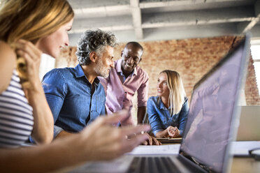 Business people with laptop discussing at desk in office - HAPF02638