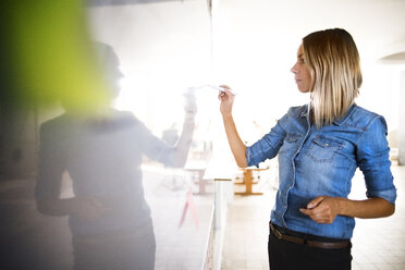 Businesswoman writing on whiteboard in office - HAPF02643