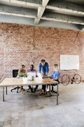 Business people with laptops discussing at desk in office - HAPF02645