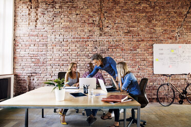 Business people with laptops discussing at desk in office - HAPF02646