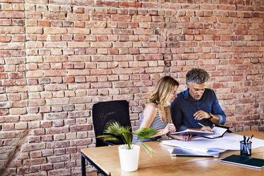 Colleagues with plan and notebook working at desk in office - HAPF02648