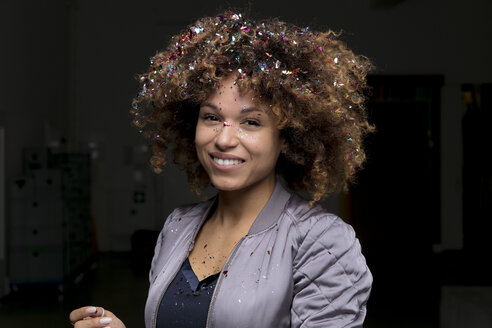 Porträt einer lachenden Frau mit Konfetti in den Haaren vor dunklem Hintergrund - HHLMF00026