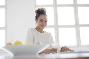 Portrait of smiling young woman sitting at table with glass of coffee - HHLMF00033