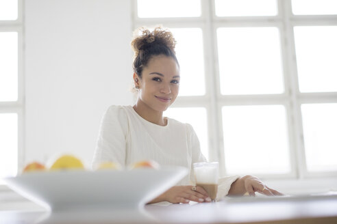 Porträt einer lächelnden jungen Frau, die am Tisch sitzt und ein Glas Kaffee trinkt - HHLMF00033