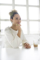 Porträt einer lächelnden jungen Frau, die am Tisch sitzt und ein Glas Kaffee trinkt - HHLMF00034