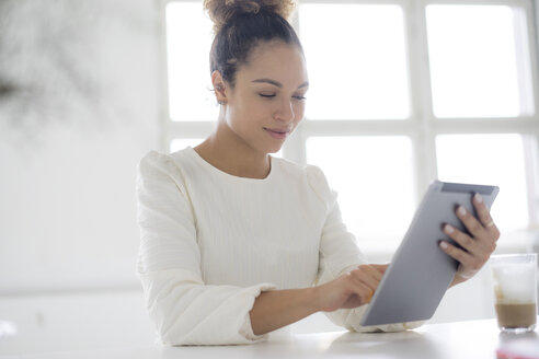 Porträt einer lächelnden jungen Frau, die ein Tablet am Tisch benutzt - HHLMF00035