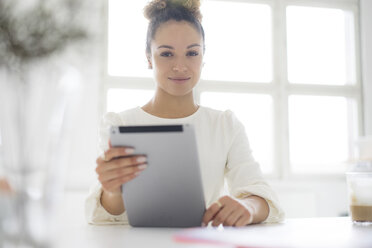 Portrait of smiling young woman using tablet at table - HHLMF00036