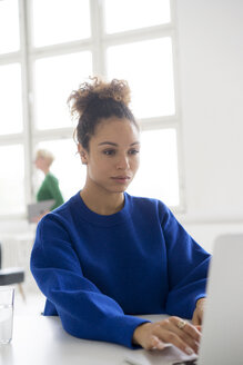 Porträt einer jungen Frau, die im Büro an einem Laptop arbeitet - HHLMF00040