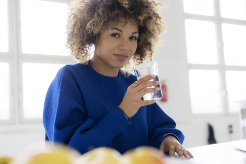 Portrait of smiling young woman drinking glass of water at table stock photo