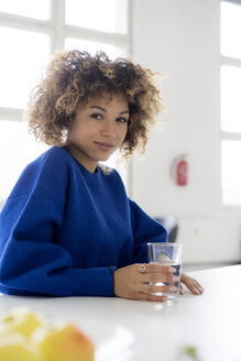 Porträt einer lächelnden jungen Frau mit einem Glas Wasser am Tisch - HHLMF00043