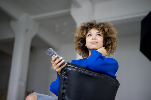 Porträt einer Frau mit Mobiltelefon auf einem Sessel sitzend - HHLMF00049