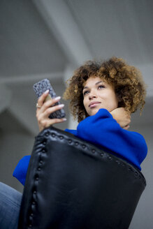 Portrait of smiling woman with cell phone sitting on armchair - HHLMF00050