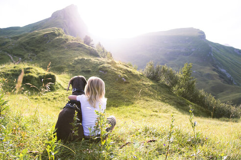 Österreich, Südtirol, junges Mädchen mit Hund auf einer Wiese sitzend - FKF02874