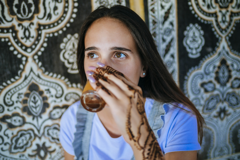 Marokko, Porträt einer Frau mit Henna-Tätowierung auf der Hand, die ein Glas Tee trinkt, lizenzfreies Stockfoto