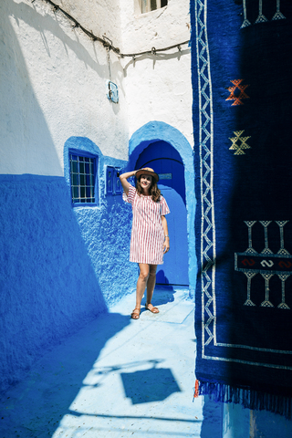 Morocco, Chefchaouen, woman standing in front of blue door enjoying sunlight stock photo