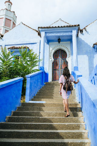 Morocco, Chefchaouen, back view of woman with backpack walking upstairs stock photo