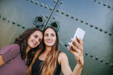 Morocco, Chefchaouen, portrait of two women taking selfie with smartphone in front of green gate - KIJF01815