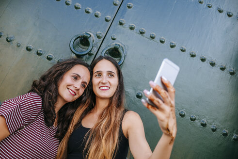 Marokko, Chefchaouen, Porträt von zwei Frauen, die vor einem grünen Tor ein Selfie mit ihrem Smartphone machen - KIJF01815