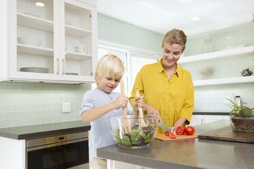 Smiling mother and son preparing salad in kitchen together - MFRF01068
